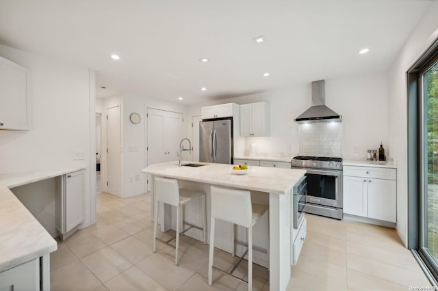 kitchen featuring white cabinetry, wall chimney range hood, stainless steel appliances, and a kitchen island with sink