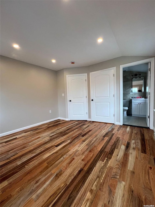 unfurnished bedroom with wood-type flooring, ensuite bath, and lofted ceiling