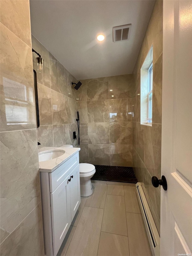 bathroom featuring a tile shower, a baseboard heating unit, toilet, vanity, and tile walls