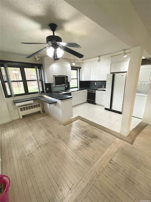 kitchen featuring stacked washing maching and dryer, light hardwood / wood-style floors, radiator heating unit, white fridge, and white cabinetry