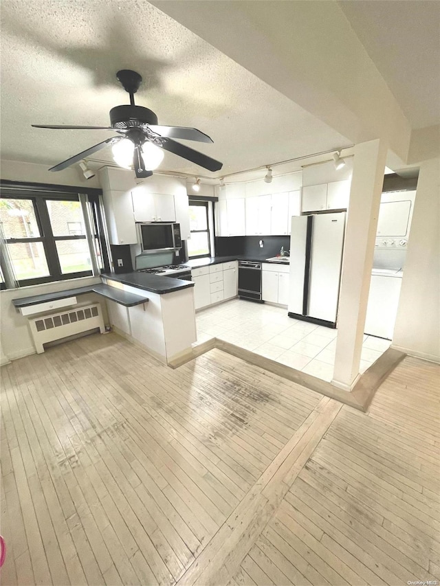 kitchen featuring light wood-type flooring, stacked washing maching and dryer, radiator, white cabinets, and white fridge