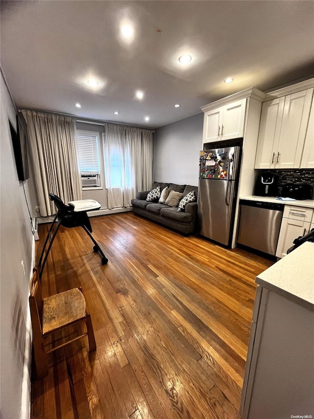 interior space with white cabinets, backsplash, stainless steel appliances, and hardwood / wood-style flooring