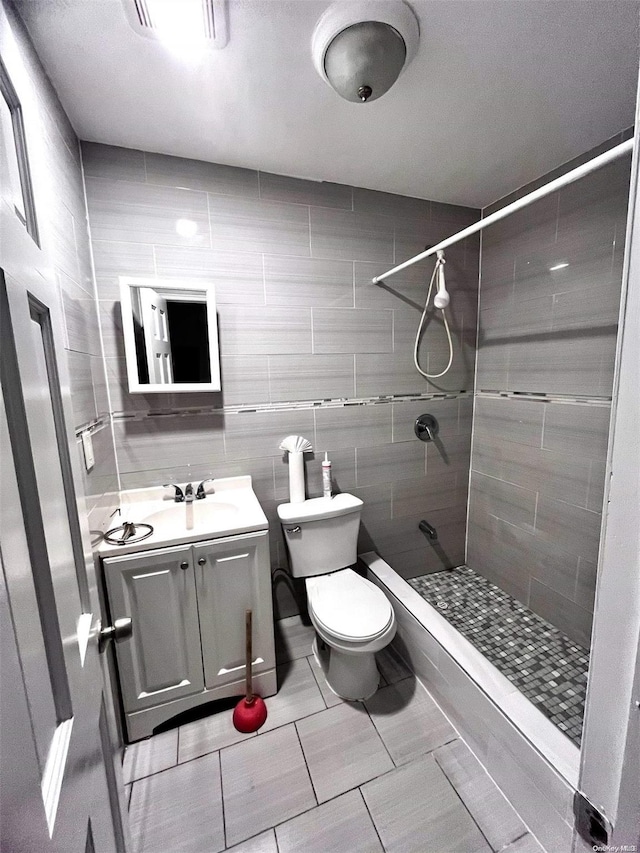 bathroom with tiled shower, vanity, toilet, and tile walls