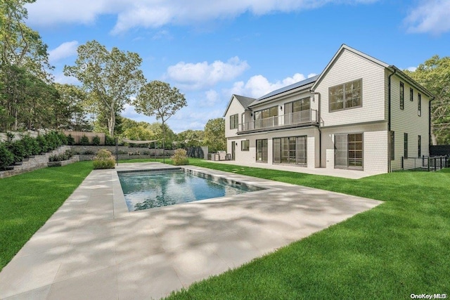 back of house with a balcony, a patio area, a fenced in pool, and a lawn