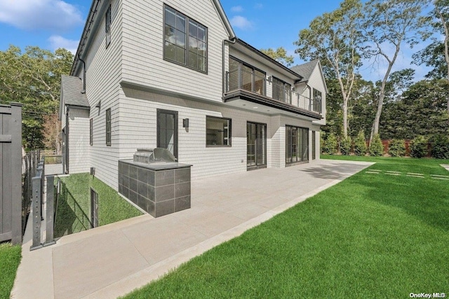 rear view of property featuring a patio area, a balcony, and a yard