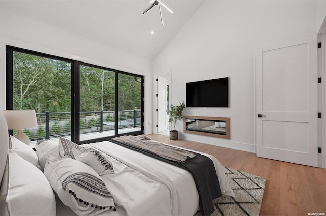 bedroom with access to outside, multiple windows, high vaulted ceiling, and light wood-type flooring