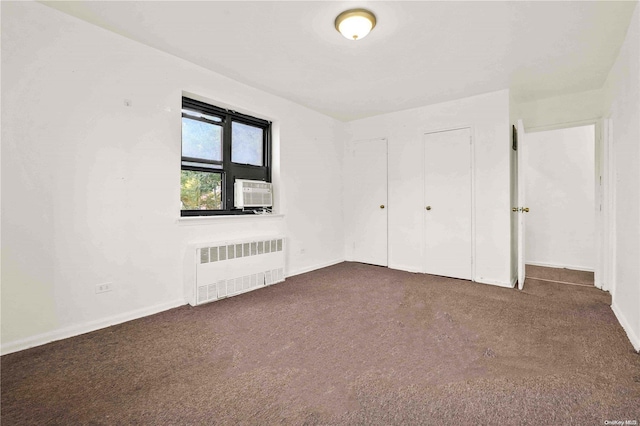 unfurnished bedroom with dark carpet, radiator heating unit, and cooling unit