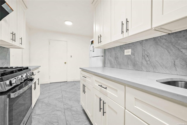 kitchen featuring tasteful backsplash, exhaust hood, white cabinets, stainless steel gas stove, and white fridge