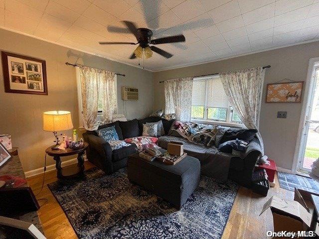 living room with wood-type flooring, a wall unit AC, ceiling fan, and ornamental molding