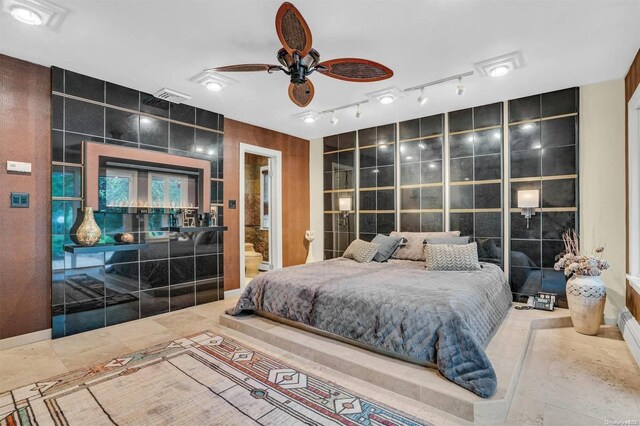 bedroom with ceiling fan, ensuite bathroom, and tile walls