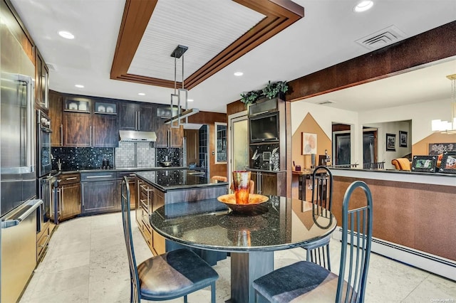 kitchen featuring hanging light fixtures, decorative backsplash, a kitchen island, a kitchen bar, and dark brown cabinetry