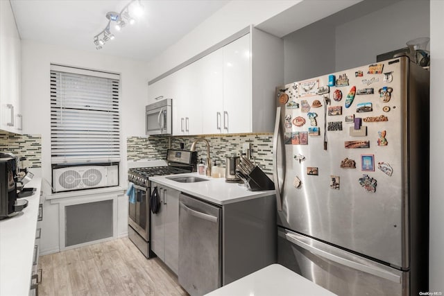 kitchen with sink, appliances with stainless steel finishes, decorative backsplash, white cabinets, and light wood-type flooring