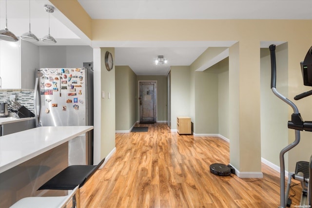 kitchen with light wood-type flooring, pendant lighting, backsplash, and stainless steel fridge