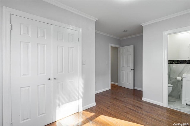 unfurnished bedroom featuring ensuite bathroom, wood-type flooring, crown molding, and a closet