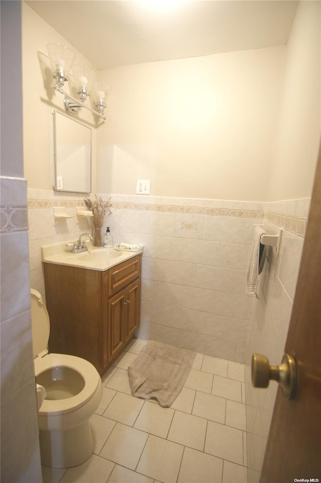 bathroom featuring toilet, vanity, tile patterned floors, and tile walls