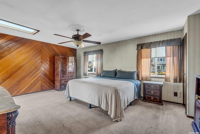 carpeted bedroom featuring ceiling fan, wooden walls, and a skylight