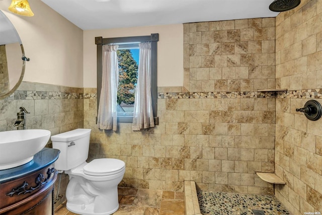 bathroom with toilet, a tile shower, tile walls, and vanity