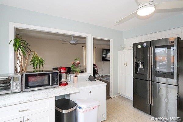 kitchen with black refrigerator, white cabinets, light stone counters, and ceiling fan