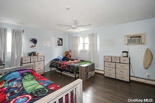 bedroom with ceiling fan, a wall mounted air conditioner, dark wood-type flooring, and a baseboard radiator