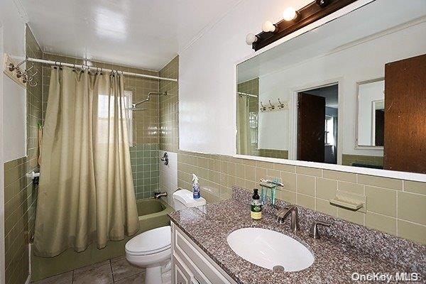 full bathroom featuring tile patterned floors, toilet, shower / bath combo with shower curtain, tile walls, and tasteful backsplash