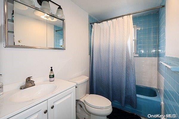 full bathroom featuring vanity, toilet, tile walls, and shower / bath combo with shower curtain