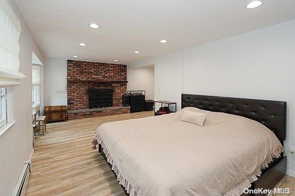 bedroom featuring a brick fireplace, light hardwood / wood-style floors, and a baseboard heating unit