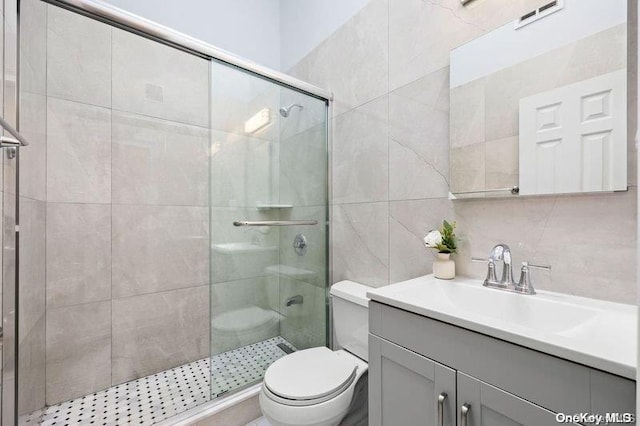 bathroom featuring vanity, toilet, tile walls, and a shower with shower door