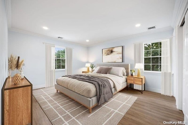 bedroom featuring multiple windows, light hardwood / wood-style floors, and ornamental molding