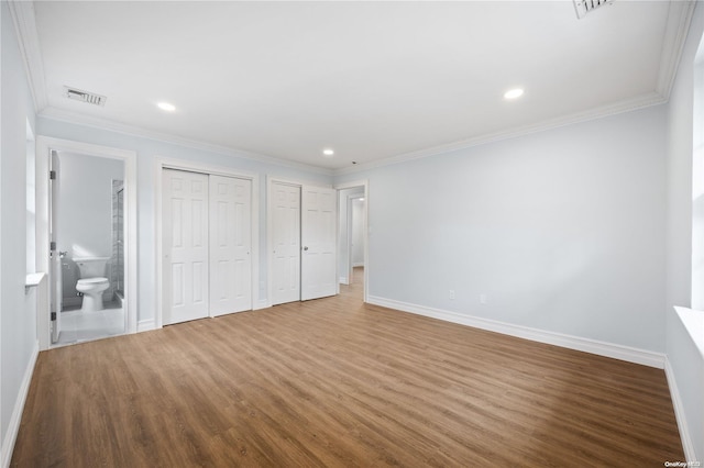 unfurnished bedroom with ensuite bathroom, wood-type flooring, ornamental molding, and multiple closets