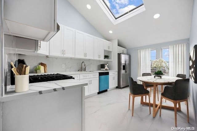 kitchen featuring appliances with stainless steel finishes, a skylight, light stone counters, sink, and white cabinets