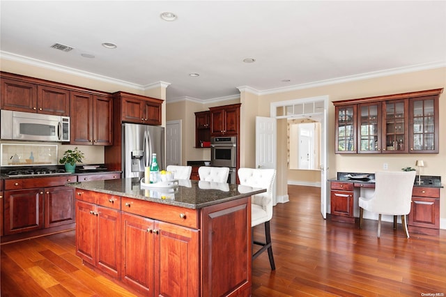 kitchen with dark hardwood / wood-style floors, dark stone countertops, a breakfast bar area, a kitchen island, and appliances with stainless steel finishes