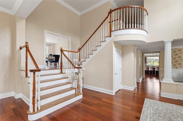 staircase featuring decorative columns, crown molding, a towering ceiling, and wood-type flooring