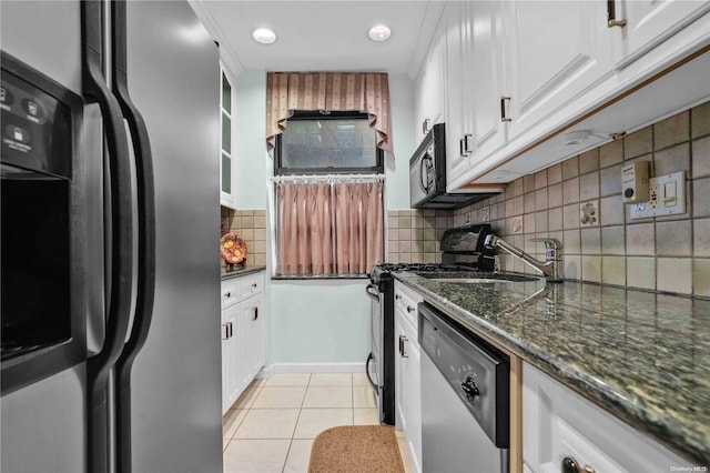 kitchen featuring stainless steel appliances, light tile patterned floors, backsplash, dark stone counters, and white cabinets