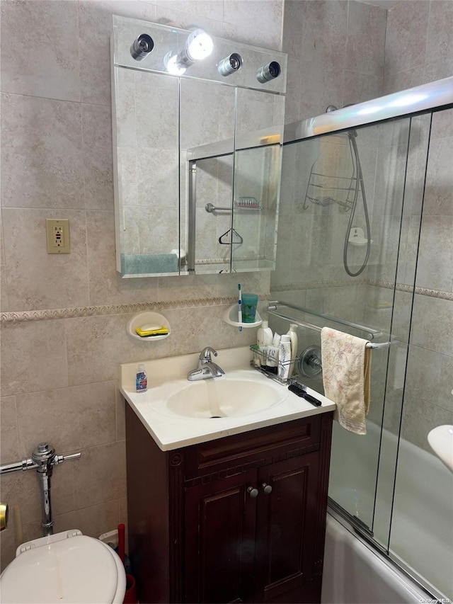 full bathroom with vanity, toilet, tile walls, and bath / shower combo with glass door