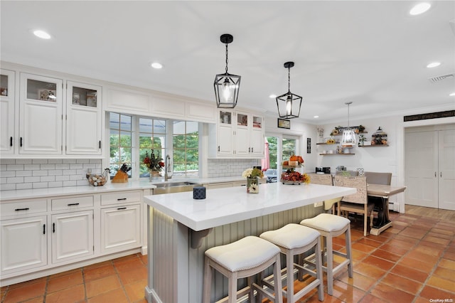 kitchen with white cabinetry, sink, decorative backsplash, a kitchen island, and ornamental molding