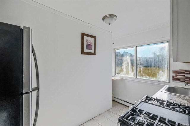 kitchen with crown molding, sink, light tile patterned floors, black range with gas cooktop, and stainless steel refrigerator