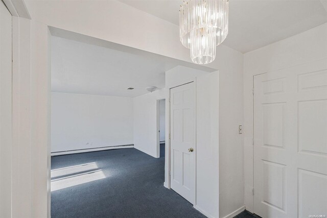 unfurnished room with dark colored carpet, an inviting chandelier, and a baseboard heating unit