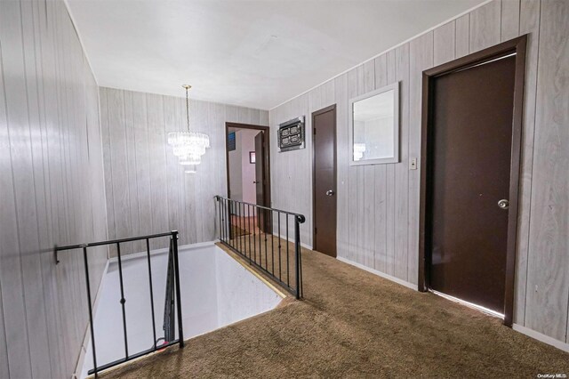 corridor featuring wooden walls, carpet, and a notable chandelier