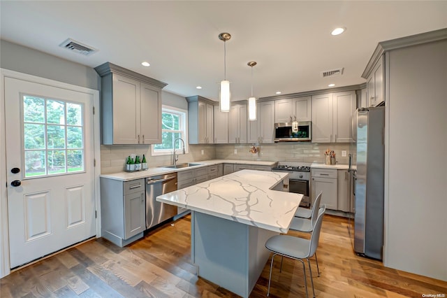 kitchen featuring appliances with stainless steel finishes, dark hardwood / wood-style flooring, sink, decorative light fixtures, and a center island