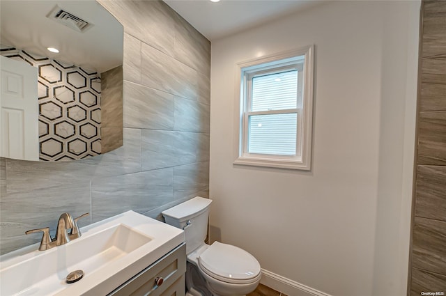 bathroom with vanity, toilet, and tile walls