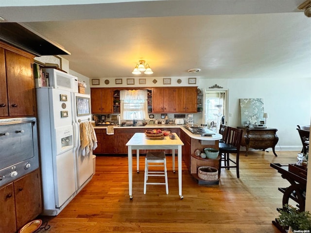 kitchen featuring sink, a kitchen breakfast bar, hardwood / wood-style floors, a chandelier, and white appliances