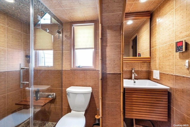 bathroom with vanity, a shower with door, toilet, and tile walls