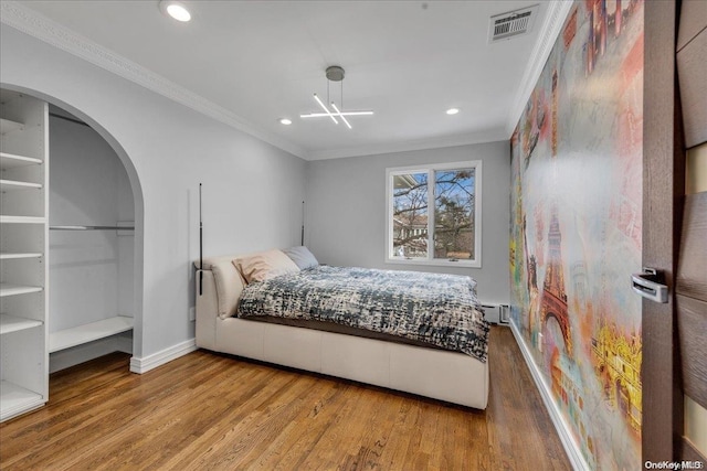 bedroom with a baseboard heating unit, hardwood / wood-style flooring, an inviting chandelier, and ornamental molding