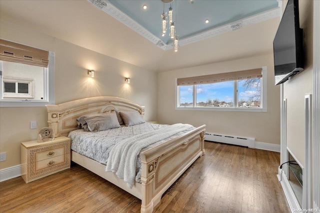 bedroom with hardwood / wood-style flooring, a raised ceiling, and a baseboard heating unit