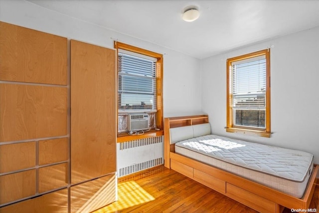 unfurnished bedroom with hardwood / wood-style floors, cooling unit, and radiator