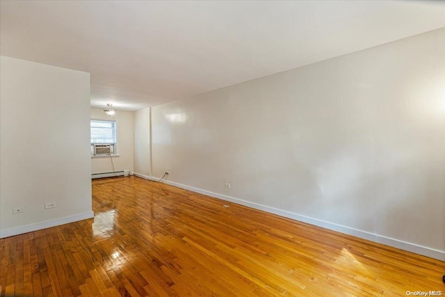 empty room featuring a chandelier, cooling unit, wood-type flooring, and a baseboard heating unit