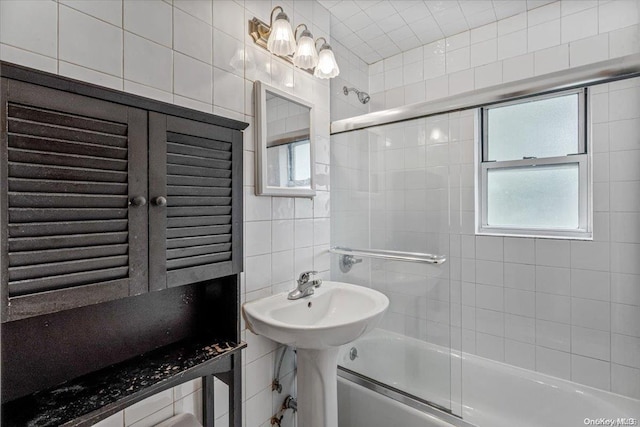 bathroom with sink, a healthy amount of sunlight, tile walls, and combined bath / shower with glass door