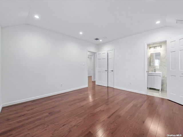 unfurnished bedroom with vaulted ceiling, wood-type flooring, and ensuite bath