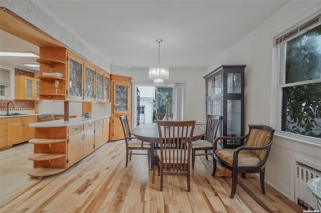 dining room with radiator heating unit, sink, crown molding, a chandelier, and light hardwood / wood-style floors