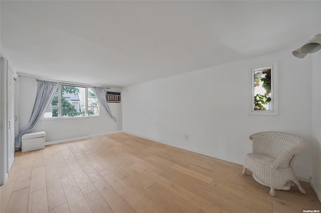 empty room with a wall mounted air conditioner, light hardwood / wood-style flooring, and plenty of natural light